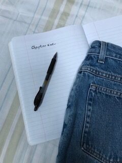 Illustration for "Pantser or Plotter?" post featuring an open notebook, pen and a pair of jeans